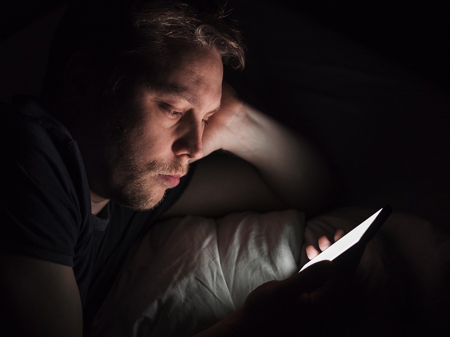 uomo con il cellulare a letto al buio